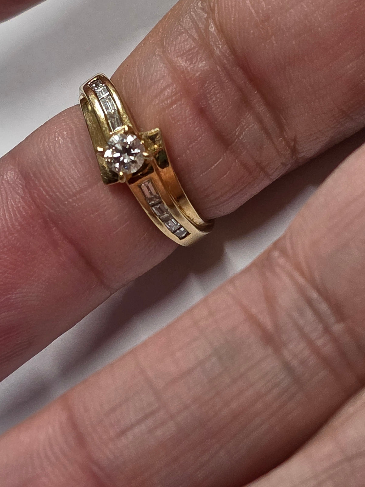 18 ct Yellow gold bypass-style diamond ring featuring a round brilliant-cut center stone flanked by channel-set baguette or rectangular accent diamonds along the Size 7