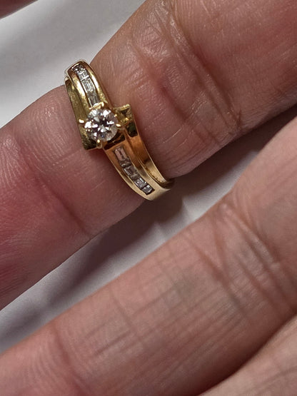 18 ct Yellow gold bypass-style diamond ring featuring a round brilliant-cut center stone flanked by channel-set baguette or rectangular accent diamonds along the Size 7