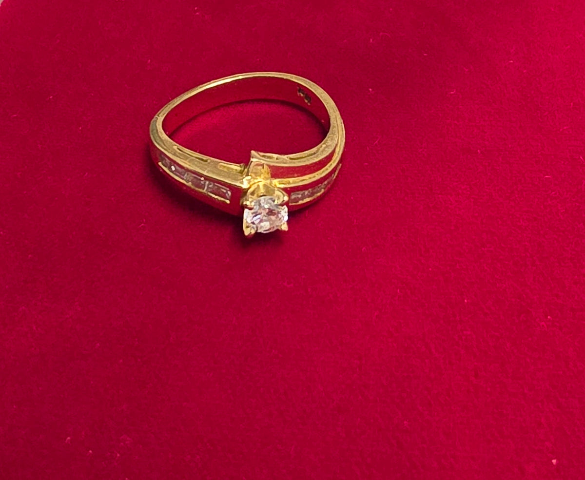 18 ct Yellow gold bypass-style diamond ring featuring a round brilliant-cut center stone flanked by channel-set baguette or rectangular accent diamonds along the Size 7