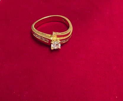 18 ct Yellow gold bypass-style diamond ring featuring a round brilliant-cut center stone flanked by channel-set baguette or rectangular accent diamonds along the Size 7