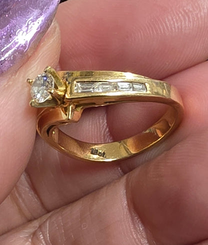 18 ct Yellow gold bypass-style diamond ring featuring a round brilliant-cut center stone flanked by channel-set baguette or rectangular accent diamonds along the Size 7
